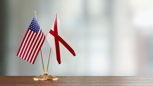 The US and Alabama state desk flags displayed together on a wooden office desk.