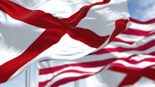 Close-up of the Alabama state flag hoisted alongside the US flag. The red cross with white background is clearly visible.