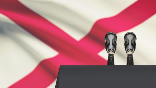 The Alabama state flag hanging behind a podium with microphones.