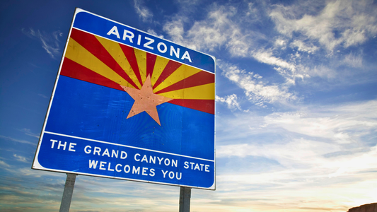 Arizona welcomes you sign next to the road displaying the flag of Arizona