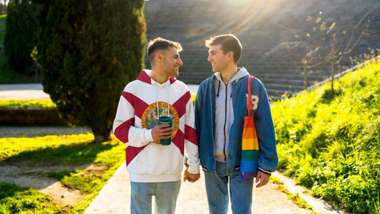 Two men walking hand in hand in a park. One of them wearing a Florida State flag hoodie. The other one a blue college jacket