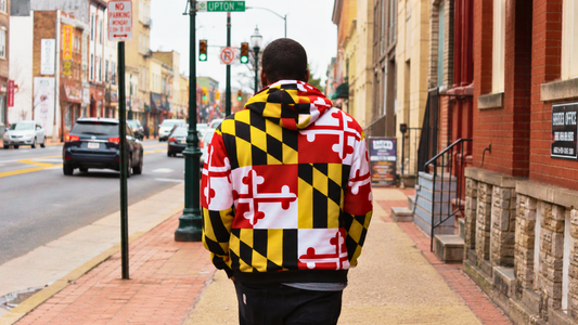 A man walking down Upton Avenue street, seen from the back, wearing a full Maryland State flag hoodie