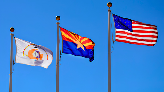 Navajo Nation, Arizona and US Flag hanging side by side, hoisted high on flag poles with clear blue skies behind it.