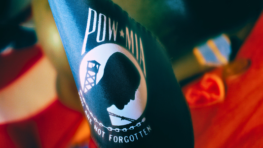 A close-up of the POW/MIA You Are Not Forgotten Flag. In the background blurred pieces of the US flag as well as military medals can be seen.