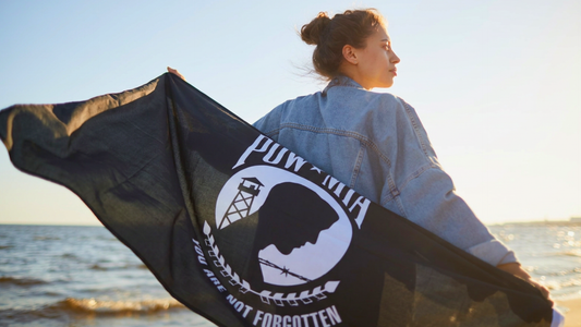 A woman standing on a beach with the stark black MIA flag draped across her back.