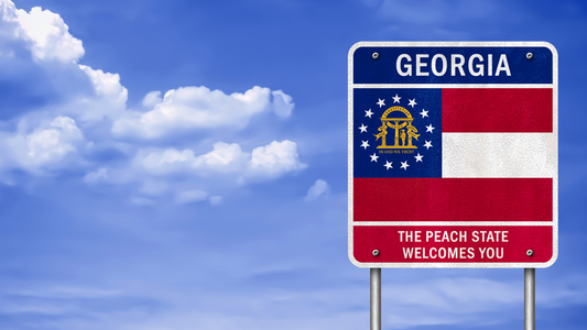 Road sign with the Georgia State Flag, with the words Georgia written above and The Peach State Welcomes You below