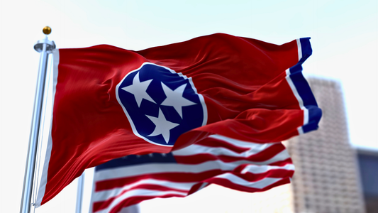The flag of Tennessee waving in the wind alongside the American flag with a high-rise visible in the background.