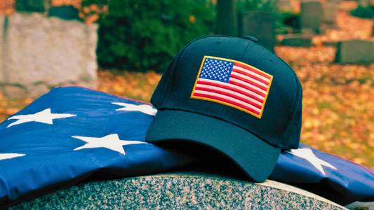 American cap with a US flag patch stitched on the front. Displayed with a folded us flag on a headstone