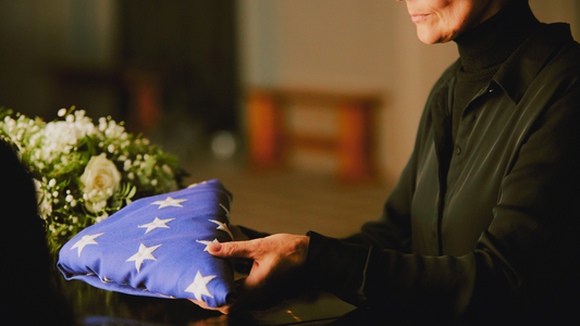 Woman wearing black holding a folded American flag over son's coffin at a funeral